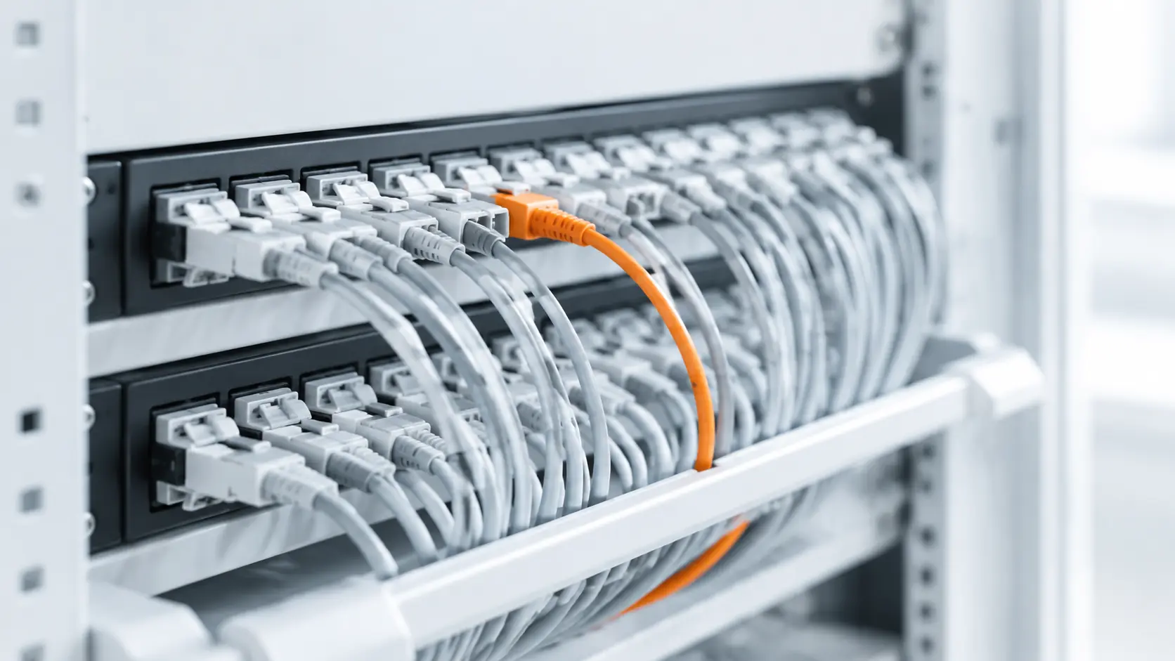 A fibre patch panel with neatly routed grey patch cords and one orange route between two rows of ports.